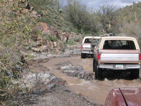 1984 Ford Bronco - A convoy of Ford Broncos navigates a water crossing on a desert trail.