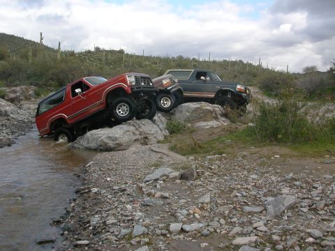 1984 Ford Bronco - Two SUVs traverse a rocky stream bed, their off-road capabilities in a , natural environment.