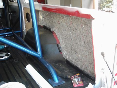 1978 Ford Bronco - The interior of a vehicle shows a partially disassembled section with insulation and a blue roll cage installed.