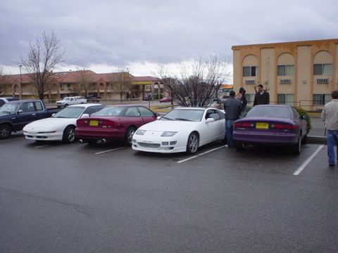 1993 Ford Probe - A group of cars are parked in a lot on an overcast day, with a hotel in the background.