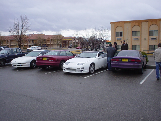 Several cars parked in a lot, including a white sports car and a purple sedan