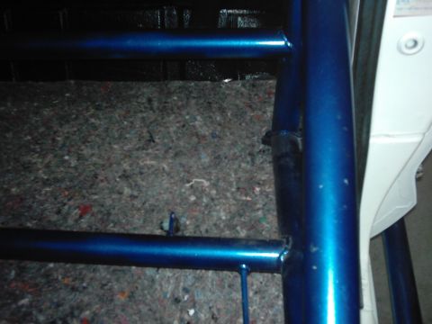 1978 Ford Bronco - Close-up view of a blue roll cage installed inside a vehicle, showing the carpeted floor and part of the door panel.