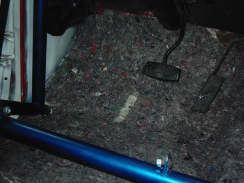 1978 Ford Bronco - Interior view of a vehicle's floor showing pedals and carpet padding, with a blue roll cage.