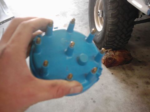1978 Ford Bronco - A blue distributor cap is held in a hand, with a vehicle tire in the background.