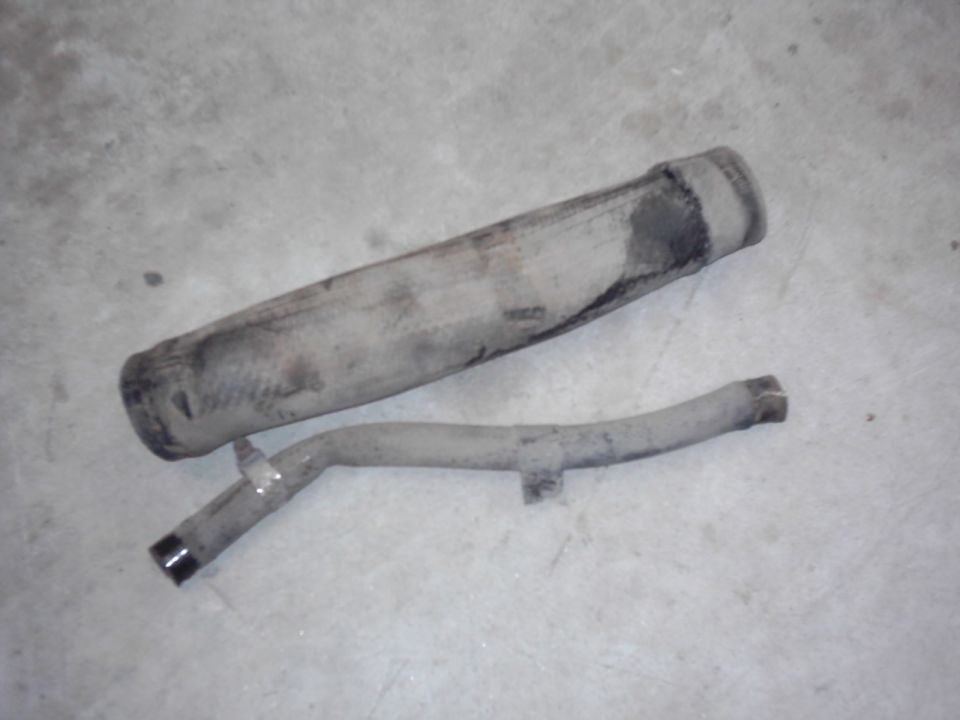 Exhaust pipe and muffler on concrete floor. The pipe is bent and has a clamp. The muffler is cylindrical and dirty