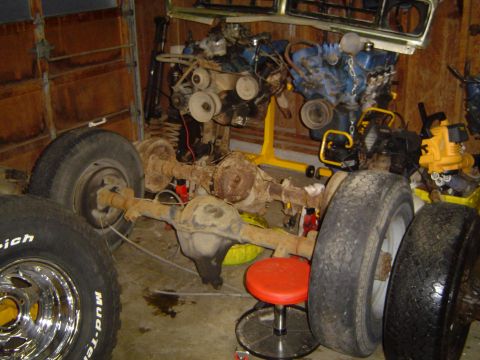 1989 Ford Bronco - Vehicle axles and engines are stored in a garage, with tires nearby.
