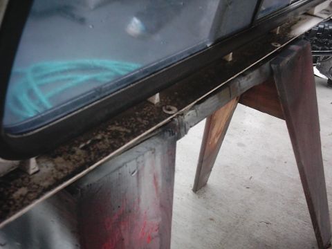 1978 Ford Bronco - A close-up shot focuses on the weathered trim and frame of a vehicle window, with a blue hose visible inside.
