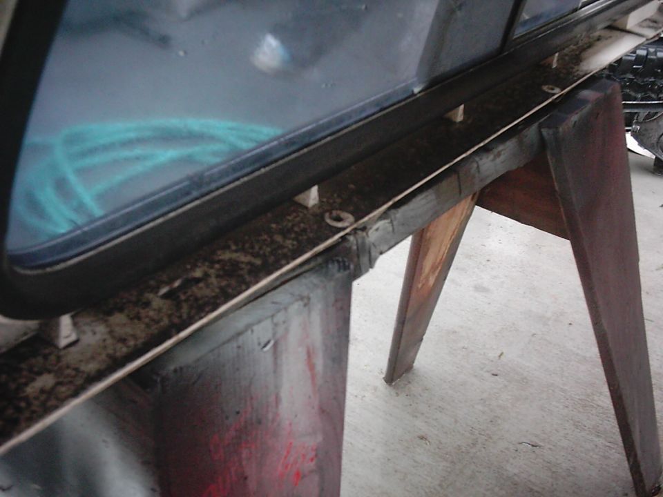 Close-up of a vehicle window frame and trim, possibly being worked on, with a blue hose visible through the glass