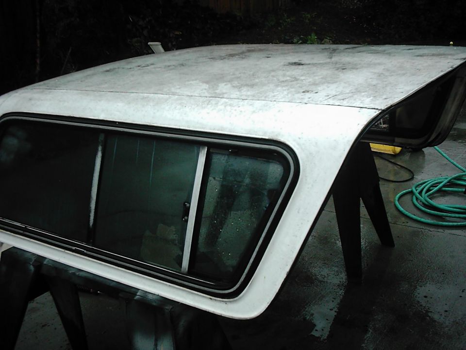 White truck bed cap with sliding window, resting on sawhorses