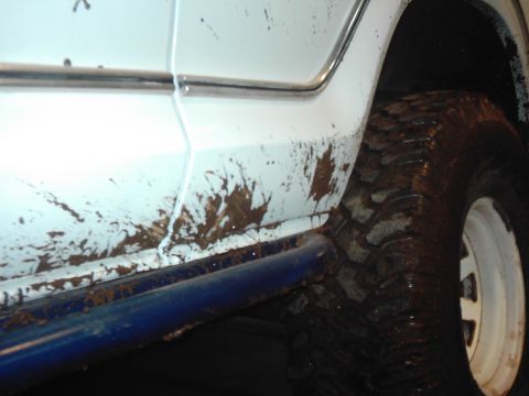 1978 Ford Bronco - Mud covers the side panel and aggressive off-road tire of a white vehicle.