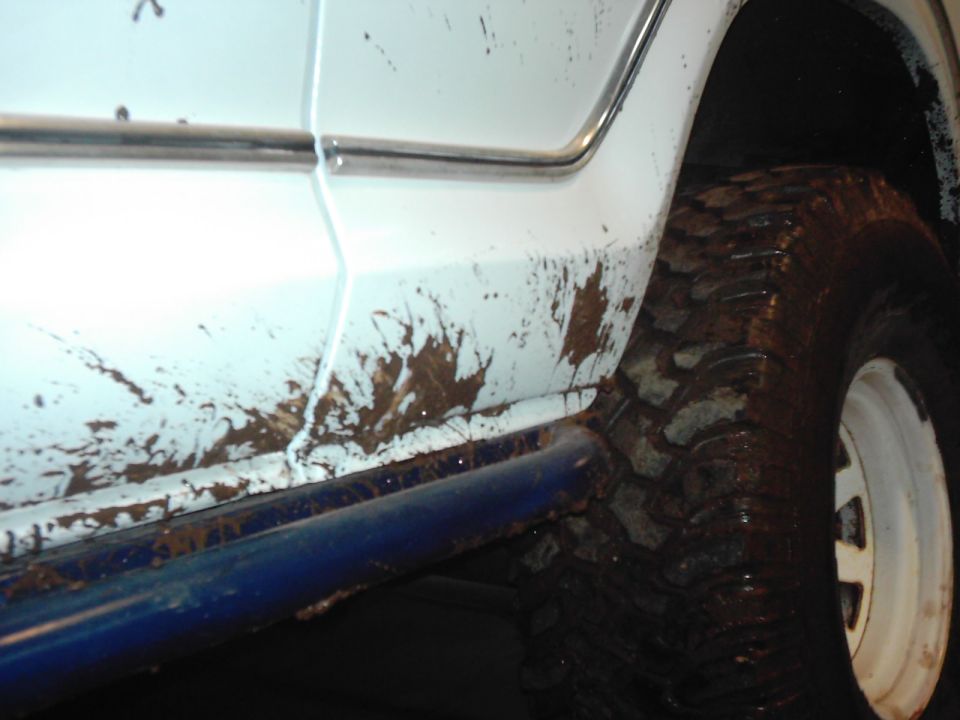 Mud splatters on the side panel and tire of a white vehicle