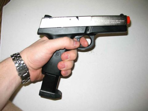 1996 Ford Taurus - A hand grips a pistol with an extended magazine and an orange tip, indicating it may be a replica or airsoft gun.
