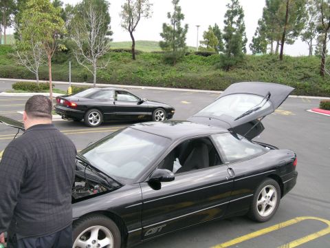 1993 Ford Probe - Two black Ford Probes are parked in a lot, with one car's hood and trunk open.