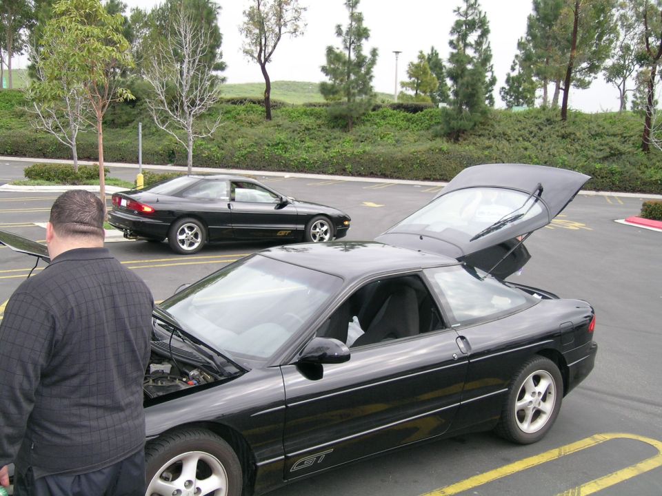 Two black Ford Probes parked in a lot, one with hood open and trunk up