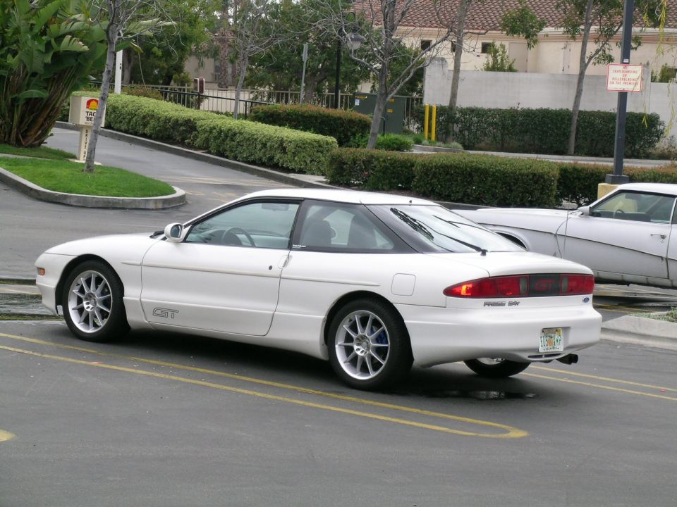 White 1993 Ford Probe GT parked in a lot, rear 3/4 view. The car has aftermarket wheels and a GT badge on the side