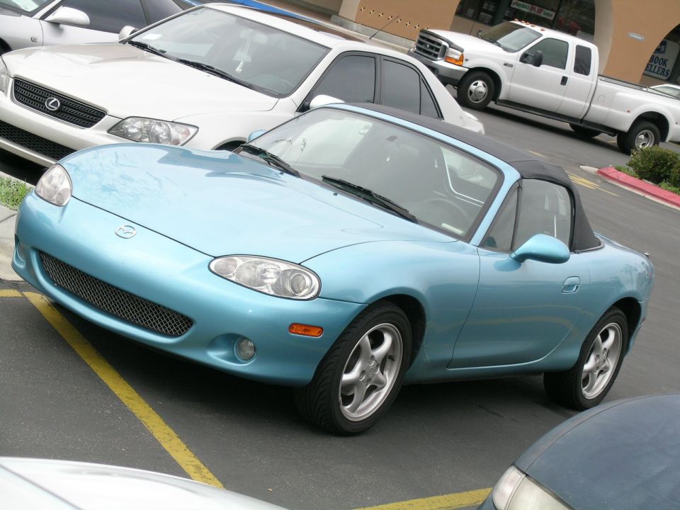 Light blue convertible sports car, front view. Likely a Mazda Miata