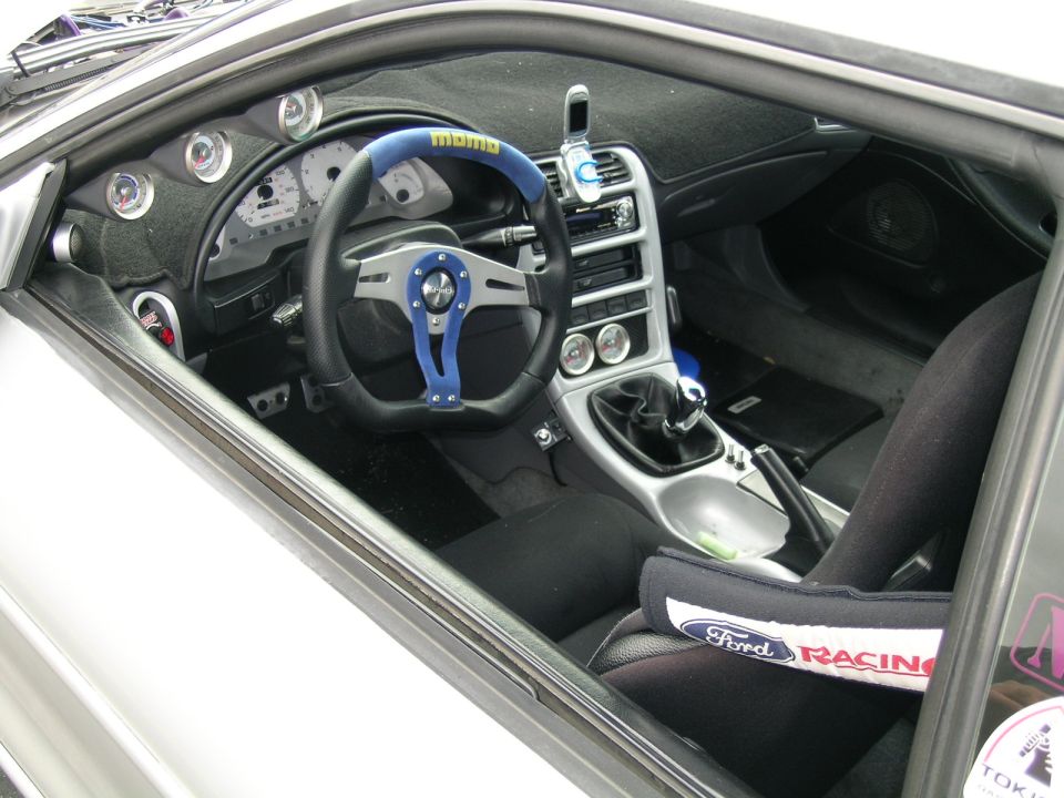 Car interior with aftermarket steering wheel, racing seat, and gauges. "Ford Racing" is visible on the seat