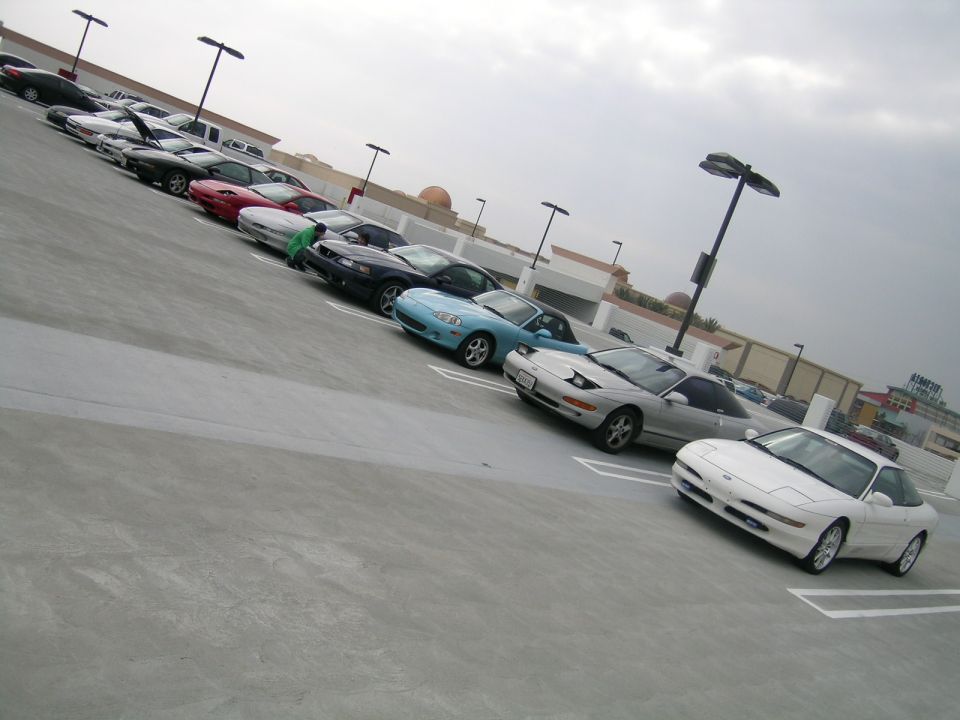 Several cars parked in a lot, including a white Ford Probe in the foreground
