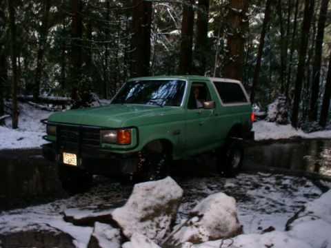 1978 Ford Bronco - Driver-side three-quarter front view of a lifted green full-size Ford Bronco with a white removable hardtop and a tubular brush guard, sitt…