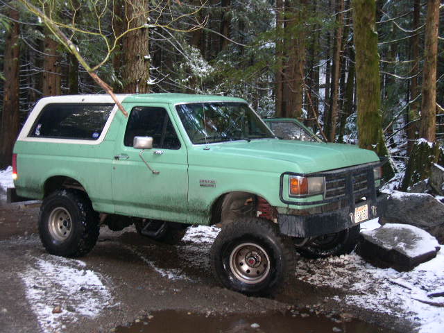 Lifted mint green Ford Bronco with white top on a snowy forest road