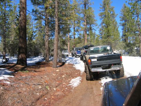 1985 Ford Bronco - A convoy of off-road vehicles navigates a dirt path through a snowy forest.