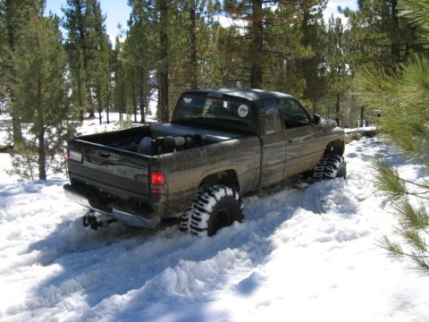 1985 Ford Bronco - Pickup truck with large tires driving through deep snow off-road.
