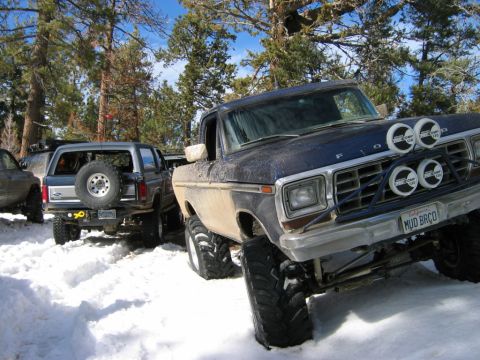 1985 Ford Bronco - Several off-road vehicles are parked in the snow, including a blue Ford Bronco.