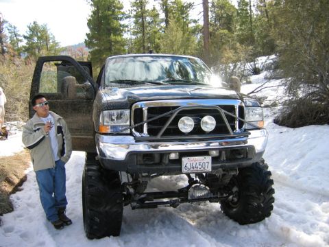 1985 Ford Bronco - Black Ford F-250 truck with custom grille guard and large tires parked in snow. A man stands beside the driver's door.