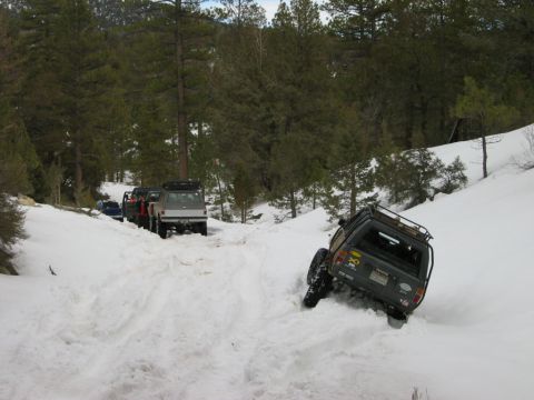 1985 Ford Bronco - Four-wheel drive vehicles navigate a snow-covered trail through a wooded mountainside.