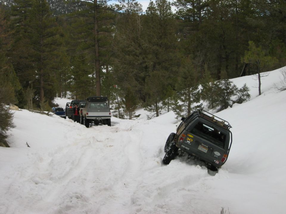 Toyota SUV tilted in deep snow on forested trail with pickup ahead