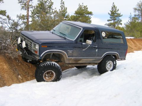 1985 Ford Bronco - This Ford Bronco is navigating a snowy, dirt embankment with its front wheels turned.