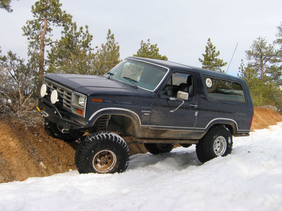 Dark blue lifted two-door Ford Bronco on snowy dirt trail with large off-road tires