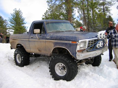 1985 Ford Bronco - A lifted, mud-covered blue Ford Bronco sits in the snow, equipped with auxiliary lights on the front bumper.