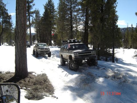 2000 Ford F-450 - Two off-road trucks are being towed through a snow-covered forest trail.