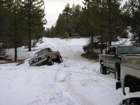 1985 Ford Bronco - A truck is stuck in the snow and a tow rope is attached to pull it out.