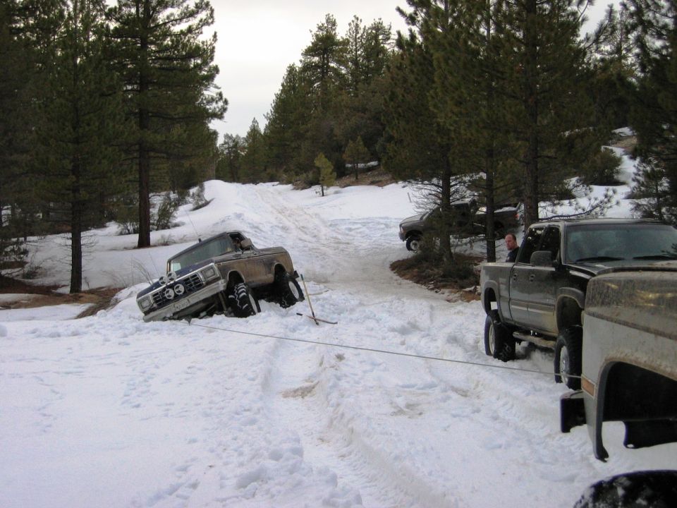 Brown Ford Bronco stuck in snow being winched by a pickup on a forest trail