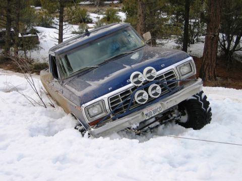 1985 Ford Bronco - A blue Ford F-Series truck is stuck in a snowy environment, with its front end partially submerged.