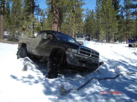 2000 Ford F-450 - A lifted Dodge Ram pickup truck is stuck in deep snow off-road, with other vehicles visible in the background.