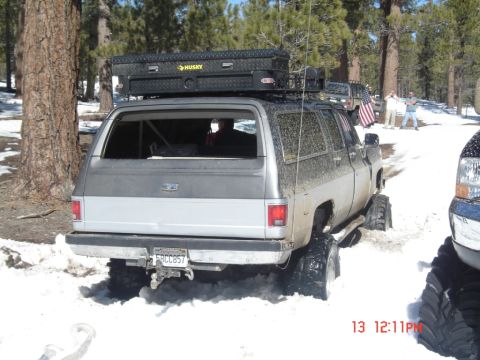 2000 Ford F-450 - A silver SUV with a large toolbox on its roof rack is stuck in the snow, with another vehicle partially visible to the right.