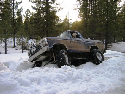 1985 Ford Bronco - Modified Ford Bronco is stuck in a snowy forest, its tires buried deep in the snow.