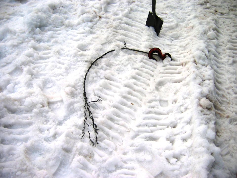 Broken frayed cable with rusty hook end on tire-tracked snow near a shovel blade