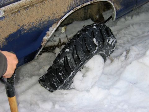 1985 Ford Bronco - Vehicle stuck in snow, a shovel is being used to clear the area around the tire.