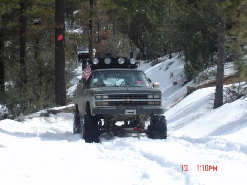 2000 Ford F-450 - A modified pickup truck navigates a snowy, wooded terrain with its front end visible.