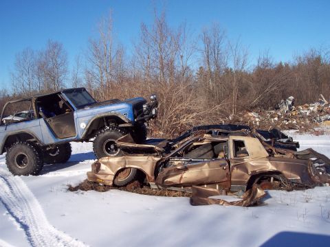 1974 Ford Bronco - A blue Bronco is parked on top of two heavily damaged cars in a snowy, wooded area.