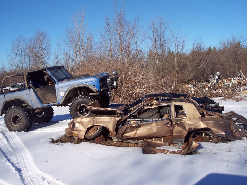 Blue Bronco on top of two crushed cars in the snow