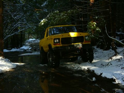 1990 Ford Bronco - A lifted yellow Ford Bronco navigates a wet and snowy forest path.