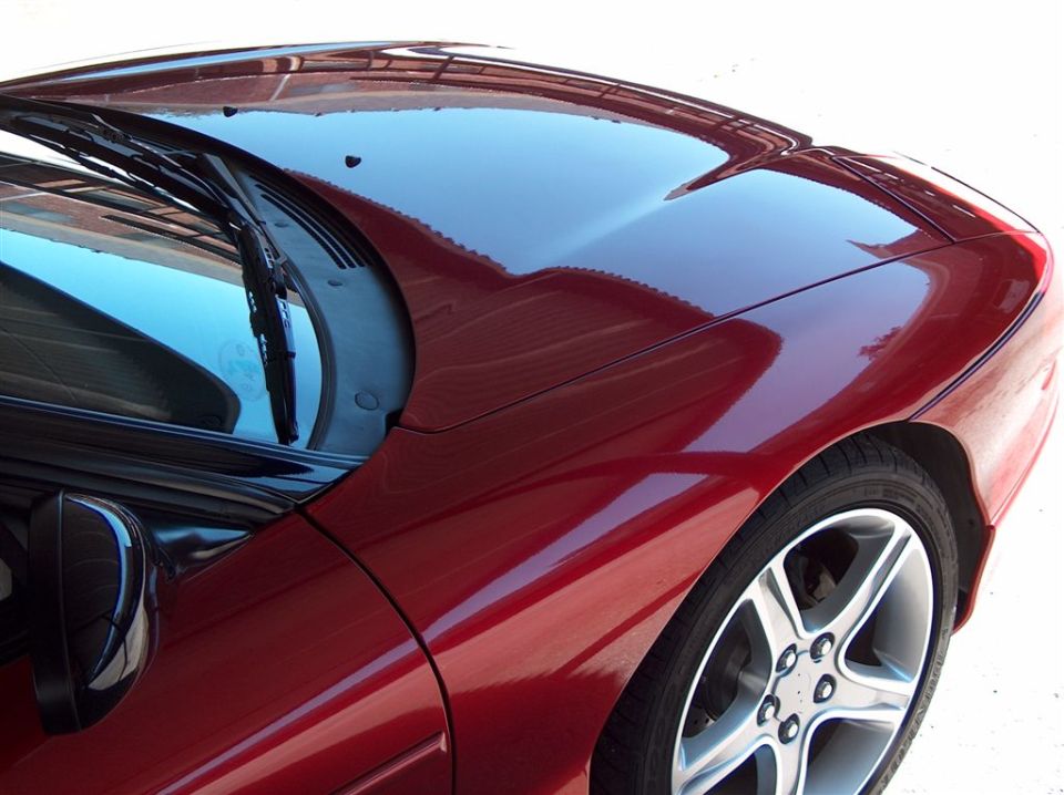 Close-up of glossy candy-red coupe fender, cowl and five-spoke alloy wheel