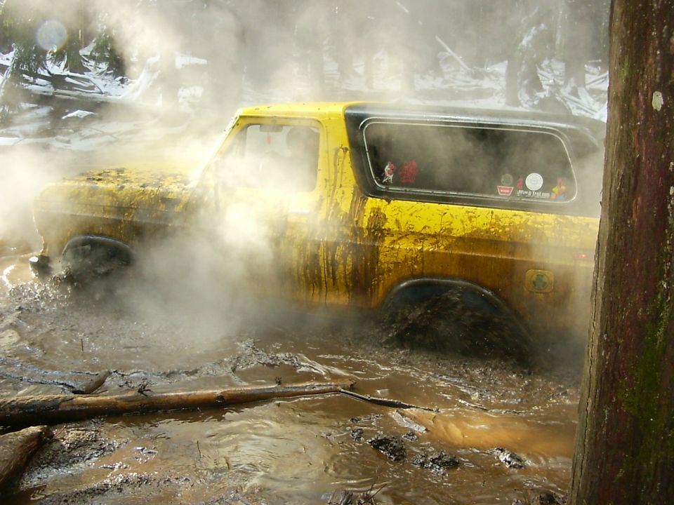 Yellow 1990 Ford Bronco stuck deep in mud with steam or smoke around it