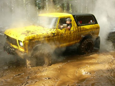 1990 Ford Bronco - Ford Bronco navigating a muddy off-road trail with steam or smoke rising.