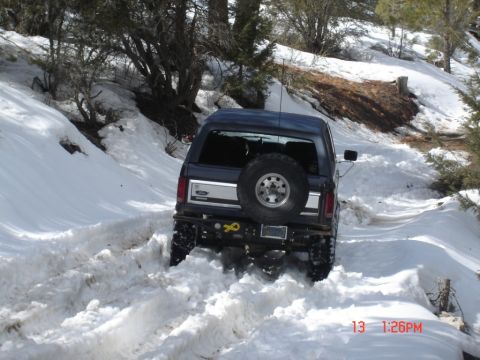 2000 Ford F-450 - A dark blue SUV navigates a snowy trail, its rear spare tire visible as it powers through the snow.
